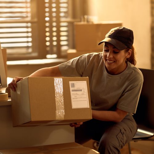 Happy delivery woman preparing cardboard boxes for a dispatch while working in the office.